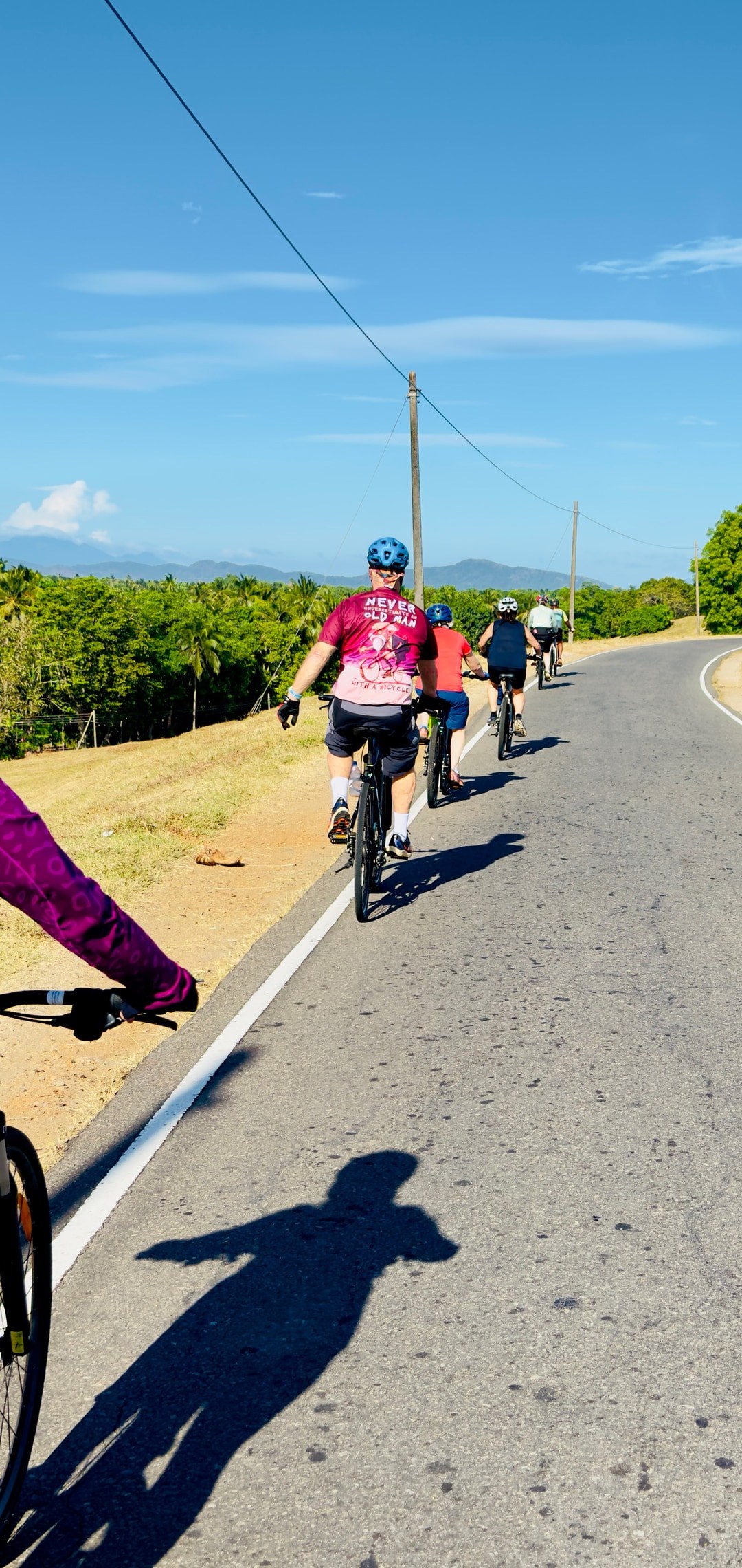 Cyclists riding along a reservoir road with mountains and tropical forest in Sri Lanka