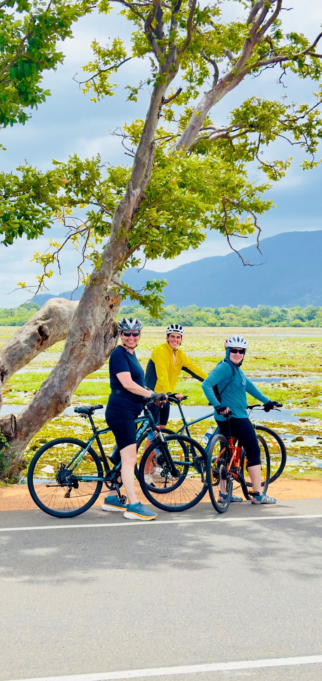 Group of cyclists on a road beside wetlands and distant mountains in Sri Lanka
