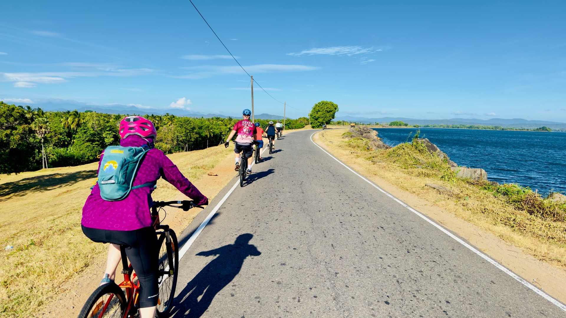 Cyclists riding along a reservoir road with mountains and tropical forest in Sri Lanka