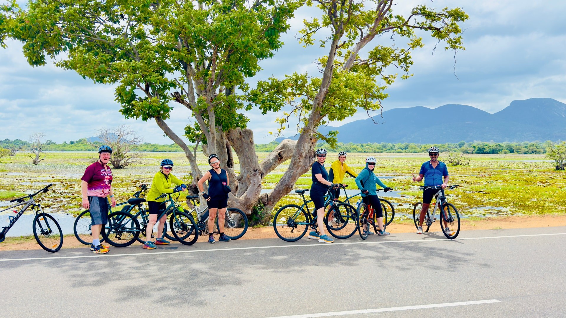 Group of cyclists on a road beside wetlands and distant mountains in Sri Lanka